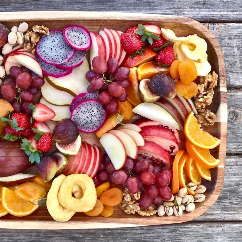 A wooden board of sliced seasonal fruit, berries and nuts
